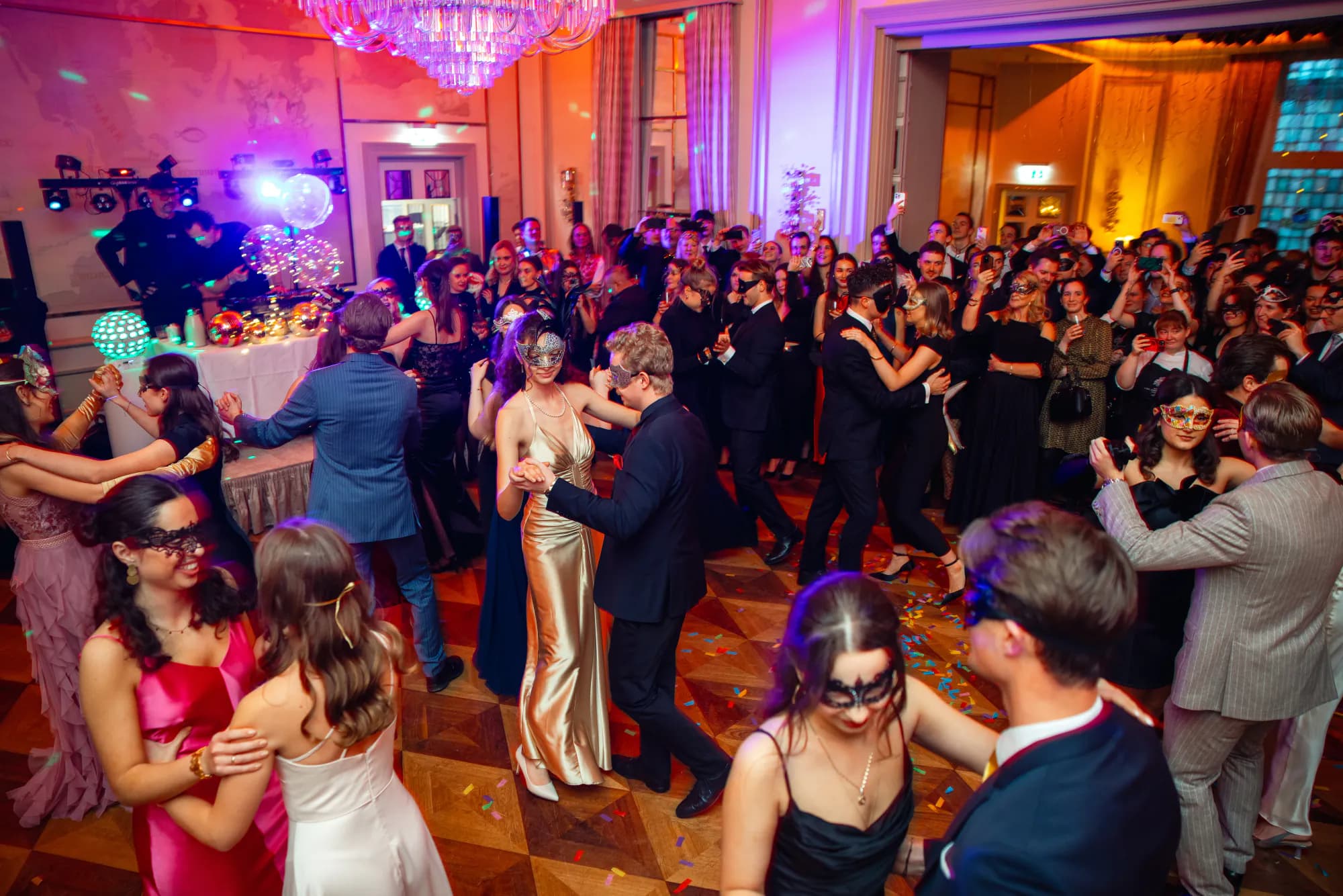 Volle Tanzfläche mit Paaren in Masken und Konfetti im Ballsaal, Weihnachtsfeier im Fairmont Hotel Vier Jahreszeiten